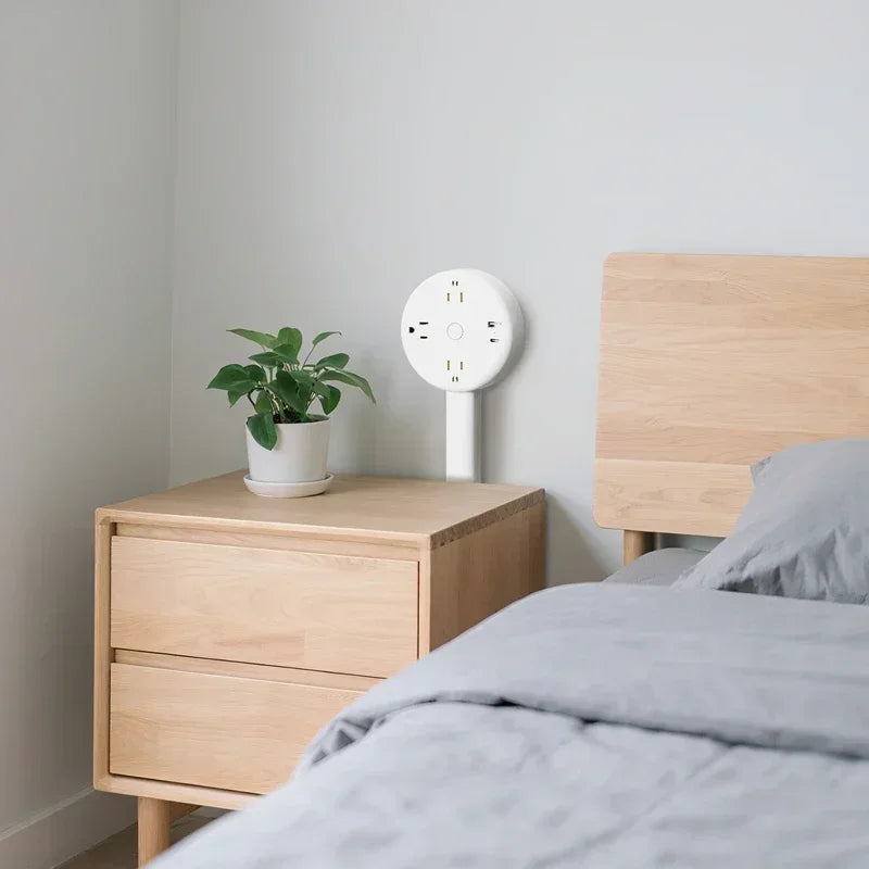 Minimalist bedroom with wooden nightstand, potted plant, and wall-mounted power strip