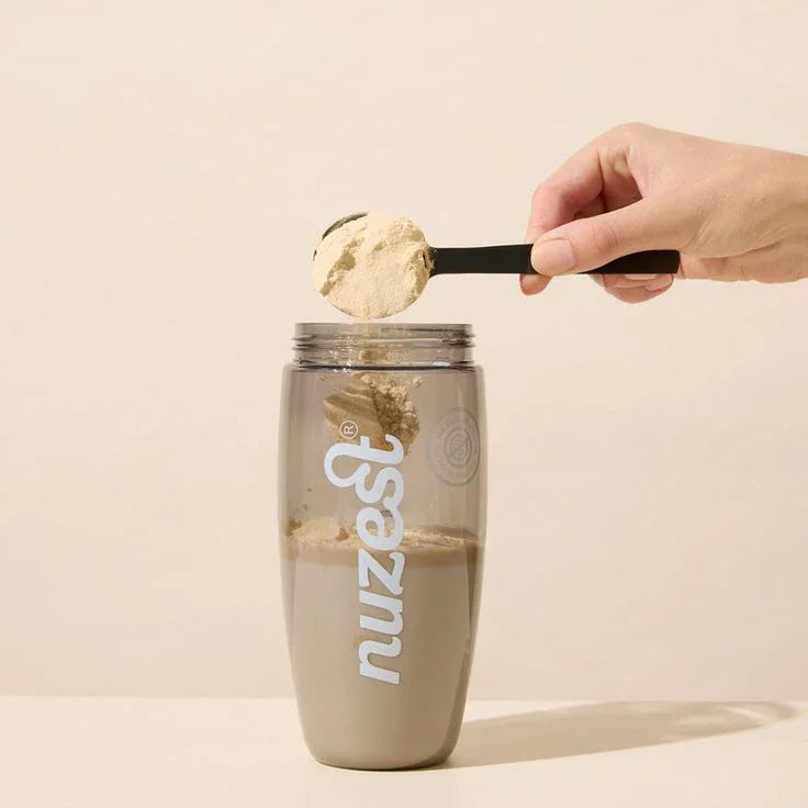 Hand scooping powder into a shaker bottle for a home wellness drink